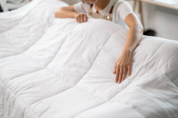 Hotel housekeeper smoothing pristine white duvet, creating welcoming bedroom environment with meticulous attention to cleanliness and guest comfort