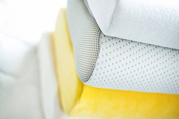 Top view of stack of soft and comfortable pillows on a bed mattress. There are three white pillows and a yellow one. Memory foam single pillows. Very shallow focus.